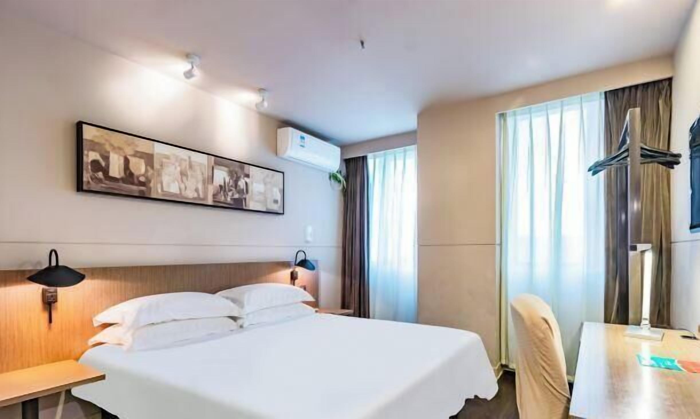 Camera d'albergo con un letto, una scrivania, una sedia, una lampada, un appendiabiti e un condizionatore d'aria a parete.