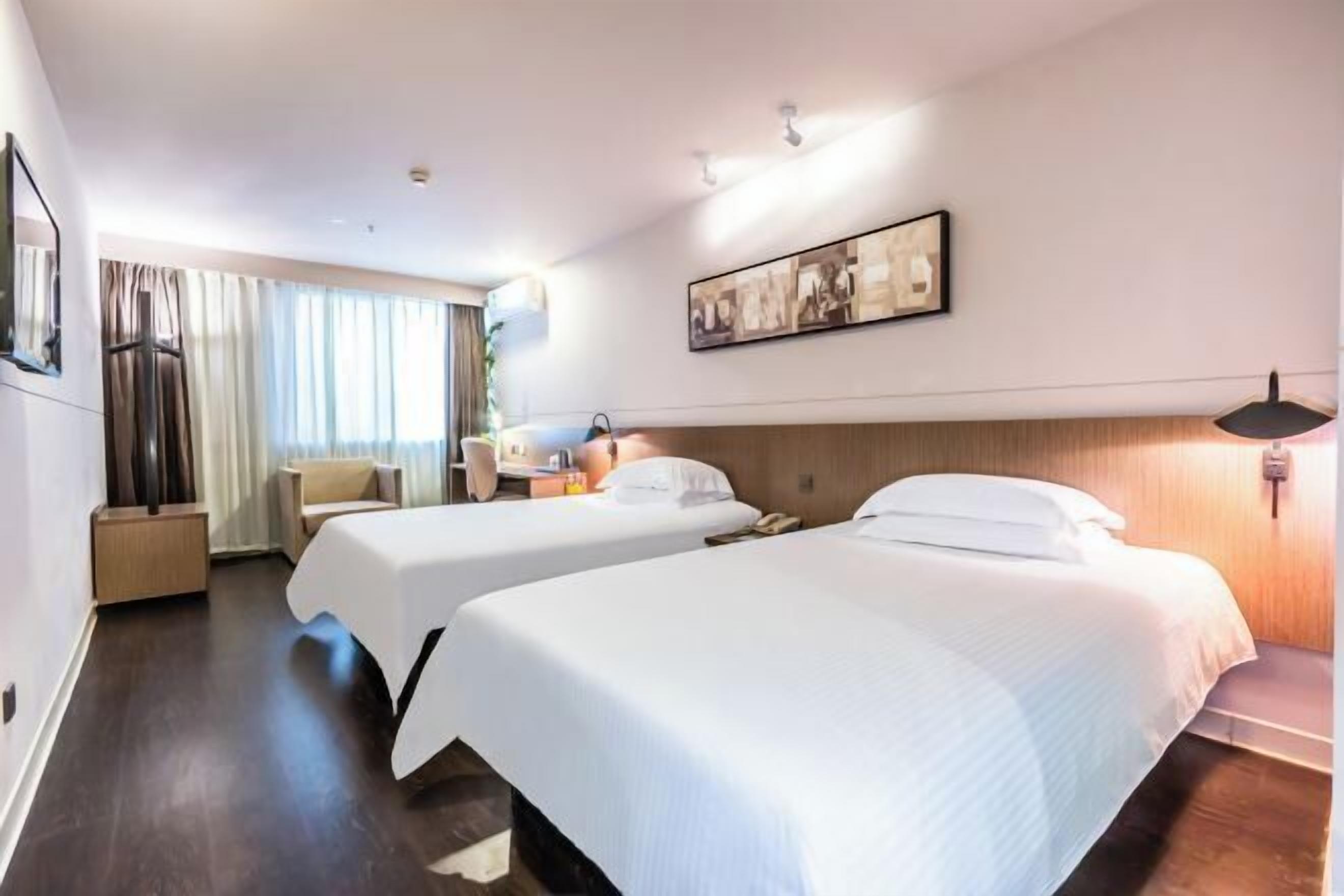Una camera d'albergo con due letti, una scrivania, una sedia, una lampada e un quadro appeso al muro.