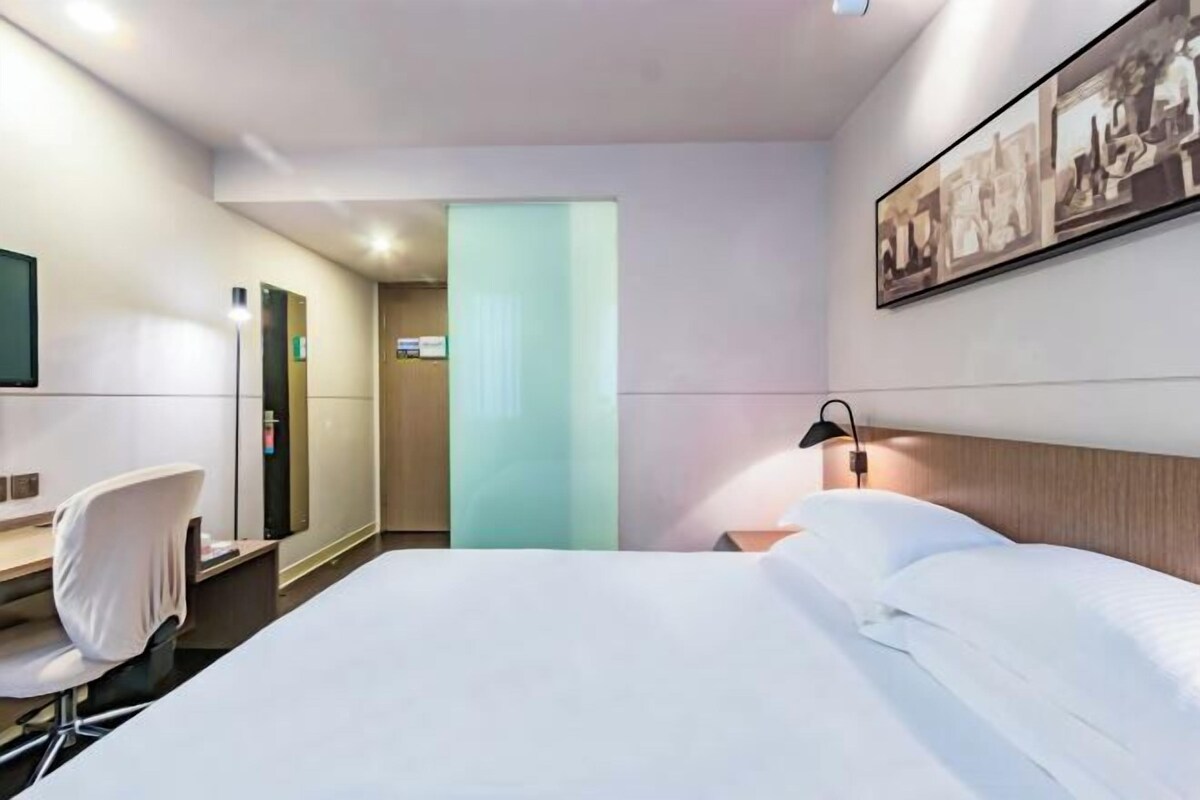 Una habitación de hotel con una cama, un escritorio, una silla, una mesita de noche y una lámpara de pared.