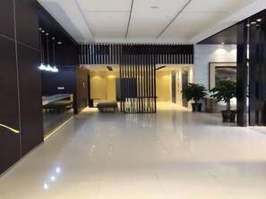 Un hall d’hôtel moderne avec un espace salon central, un comptoir d’accueil et une grande plante en pot.