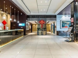 Un hall d’hôtel comprenant un comptoir d’accueil, un espace salon et un mur décoratif agrémenté d’un ornement rouge.