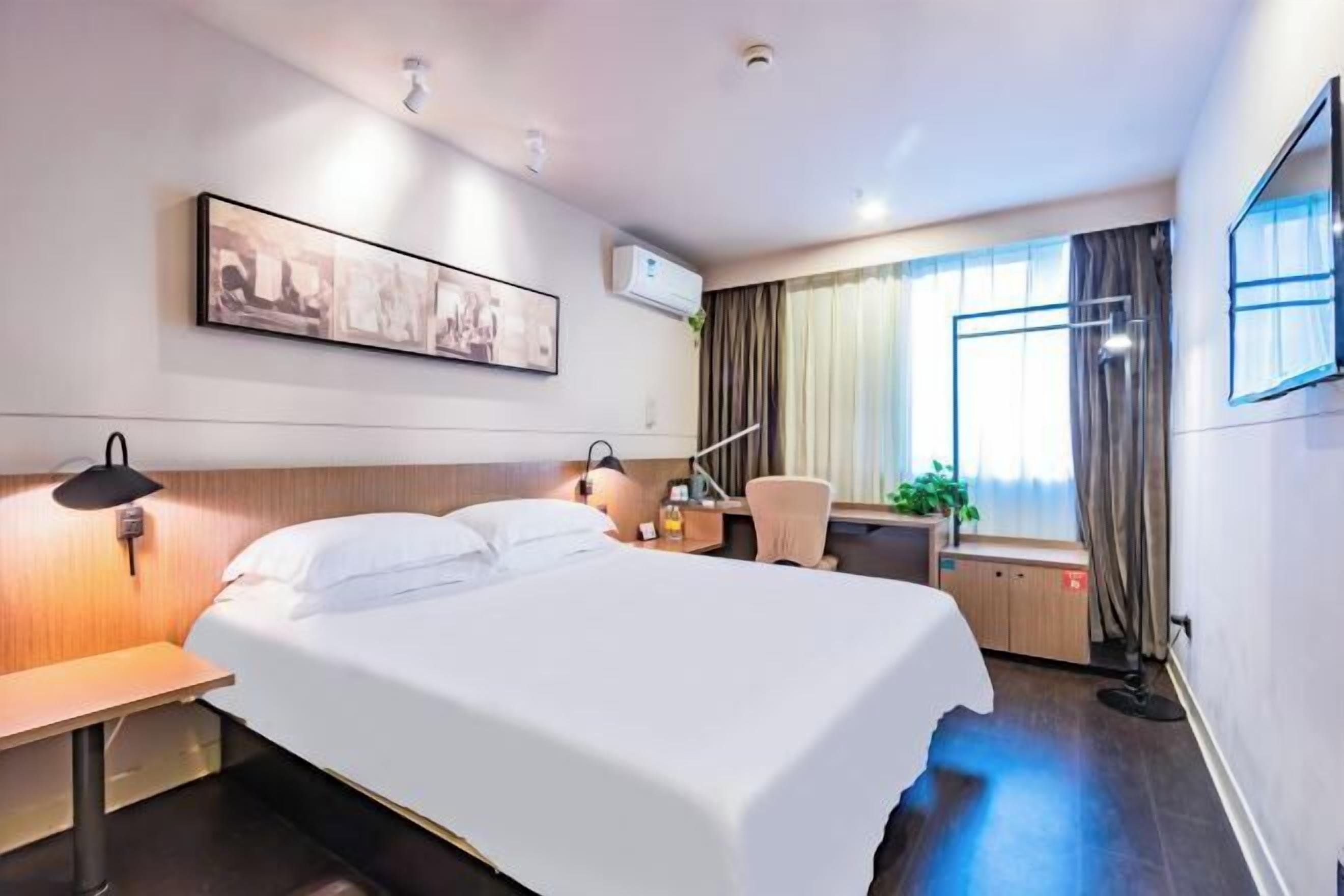 Una camera d'albergo con un letto, una scrivania, una sedia e una finestra con tende.