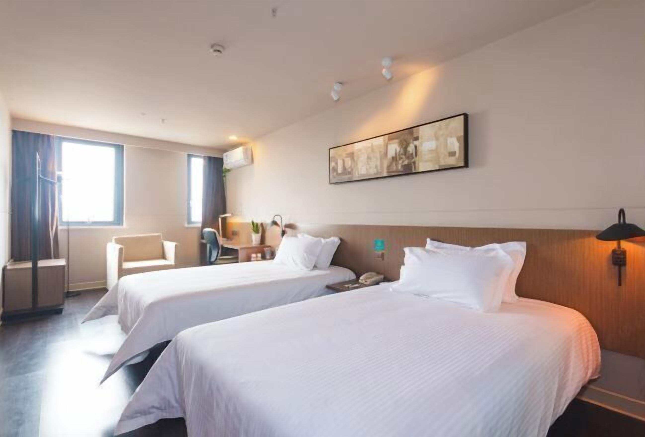 Una habitación de hotel con dos camas, un escritorio, una silla y un ventanal grande.