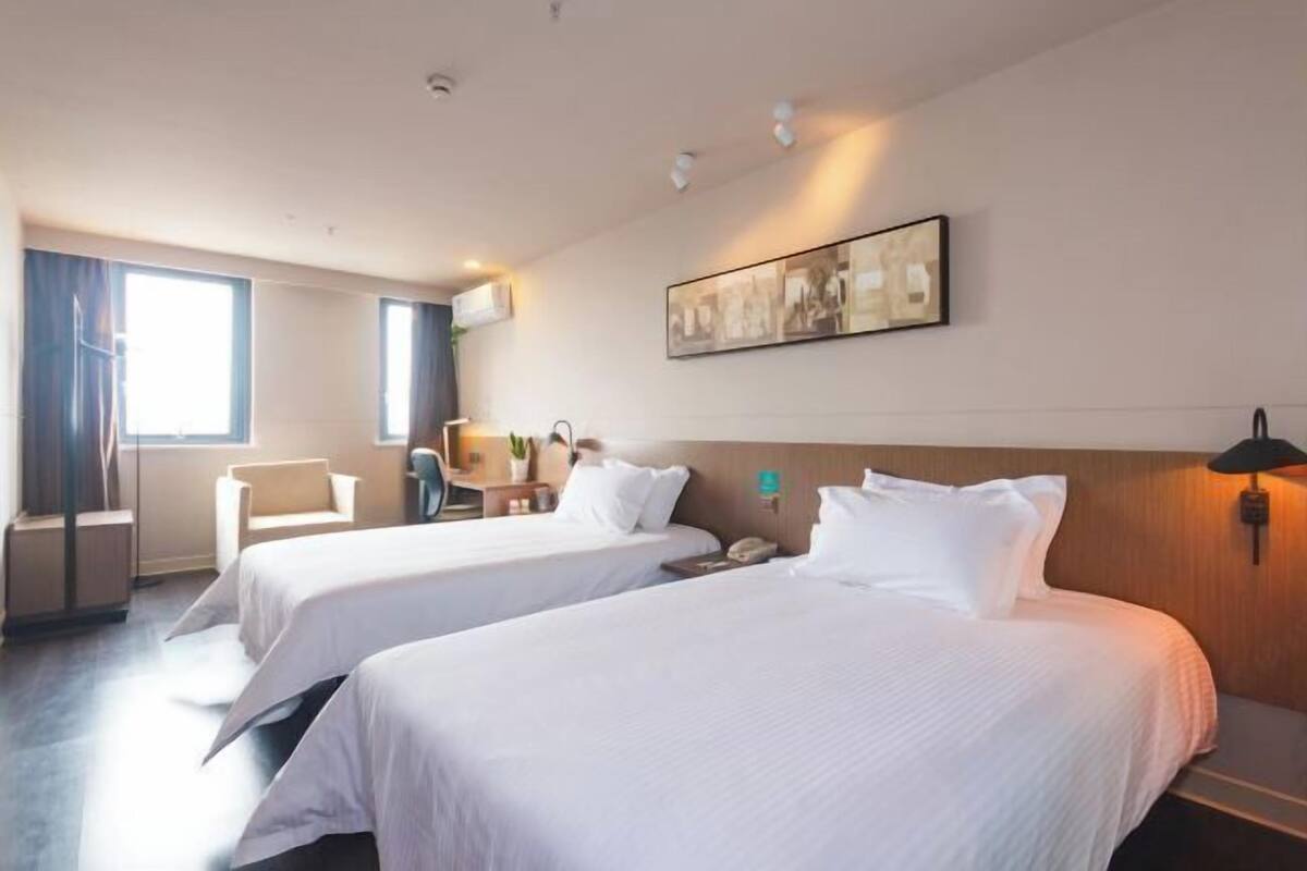 A hotel room with two beds, a desk, a chair, and a large window.