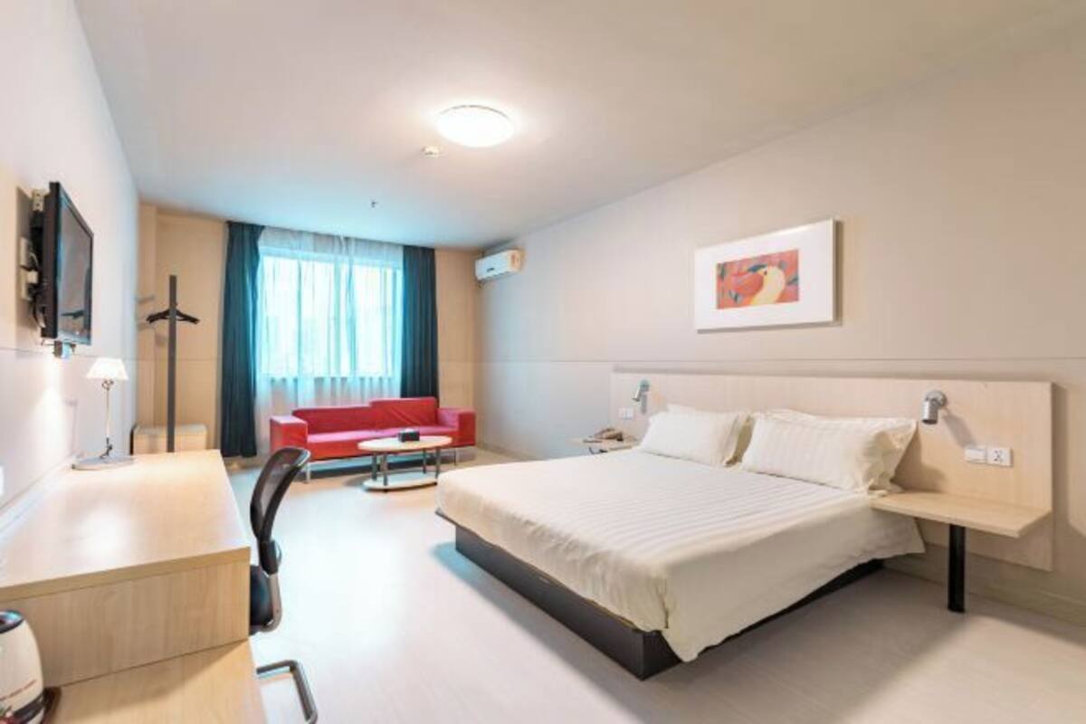 Habitación de hotel con cama, escritorio, silla, sofá rojo y televisor.