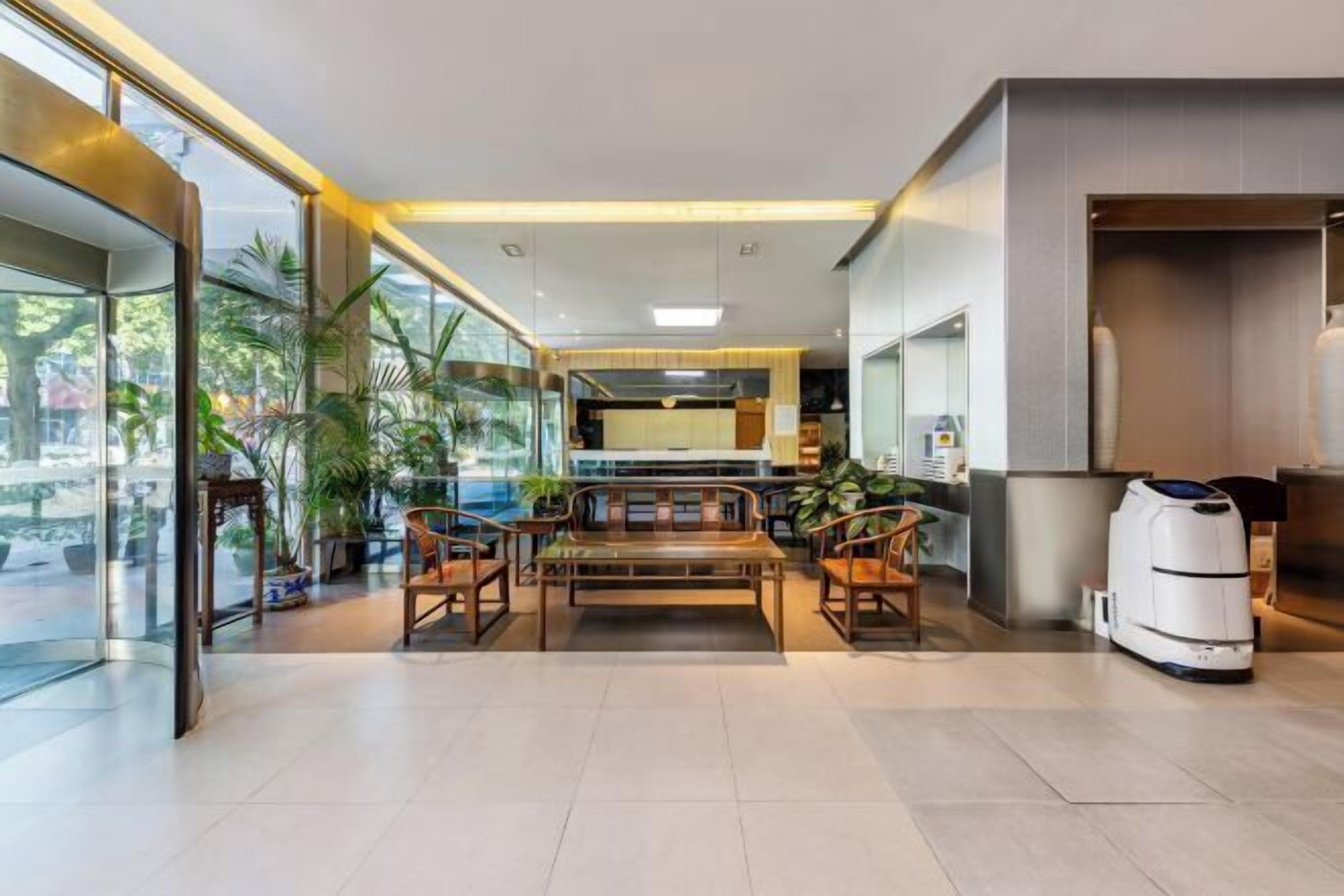 A modern hotel lobby with a seating area, a reception desk, and a large window offering a view of the outdoors.
