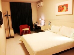 Habitación de hotel con una cama grande, un escritorio con una silla, un sillón rojo, una cortina negra y un equipo de aire acondicionado.