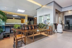 A modern interior with a dining area featuring a glass-top table and wooden chairs, a kitchen area with a large island, and a view of the city through large windows.
