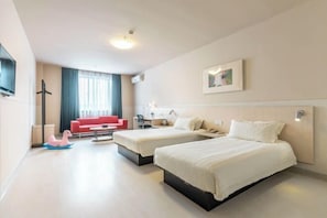 Habitación de hotel con dos camas, un sofá rojo, un escritorio y una ventana con cortinas.