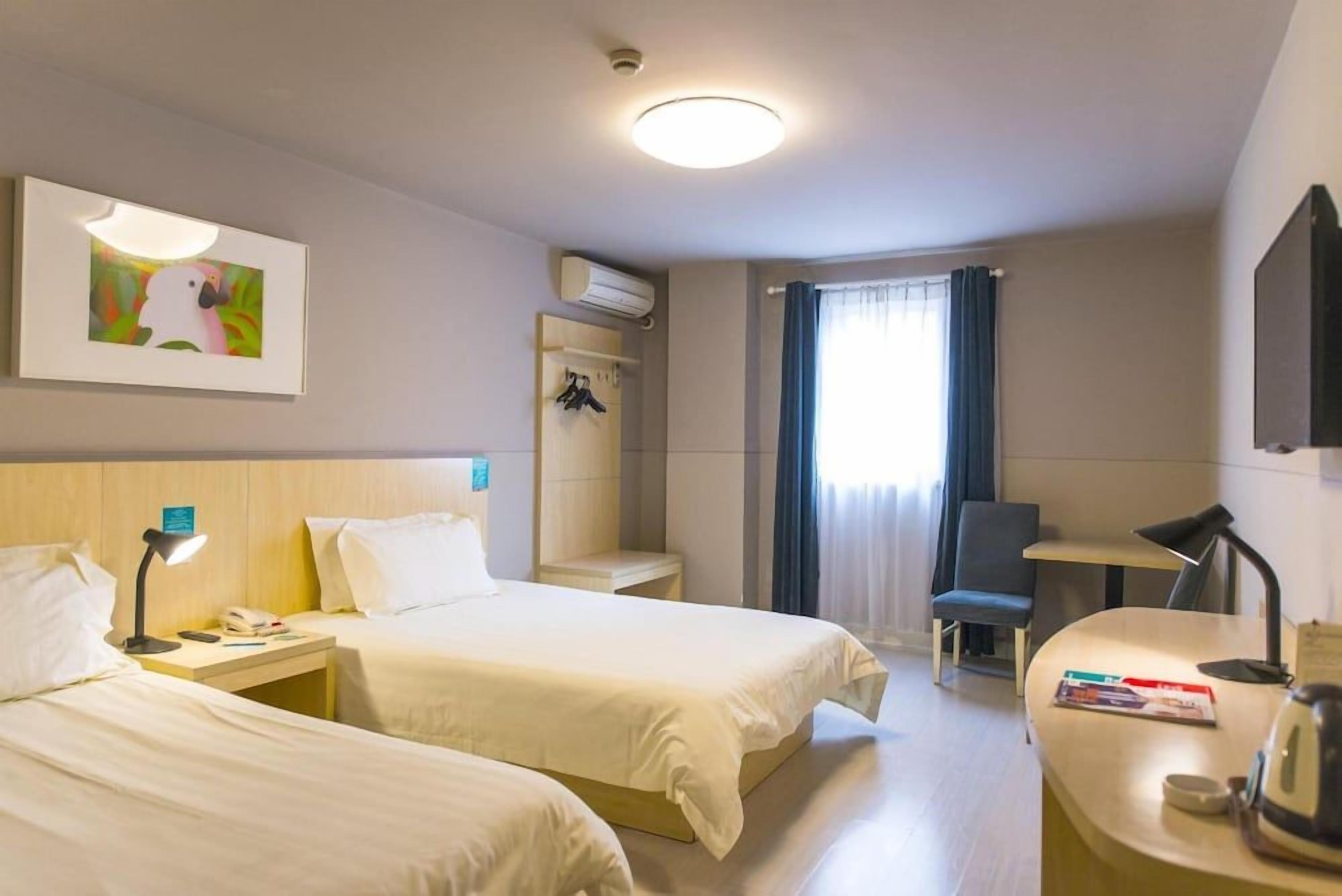 A hotel room with two beds, a desk, a chair, a picture on the wall, and an air conditioning unit.