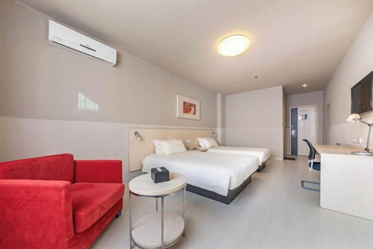 Habitación de hotel con cama, sofá rojo, una mesita redonda, escritorio y televisor.