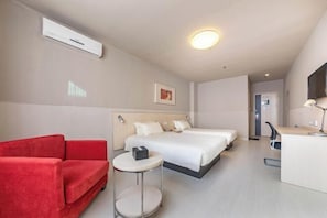 Una habitación de hotel con una cama, un sofá rojo, una mesita redonda pequeña, un escritorio y un televisor.
