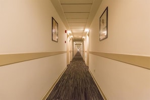 Un pasillo largo y estrecho en un hotel, con pisos alfombrados y paredes de color claro.