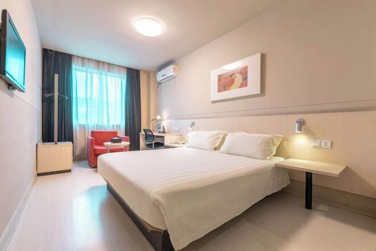 Une chambre d’hôtel avec un grand lit, un bureau avec une chaise, une télévision et un tableau au mur.
