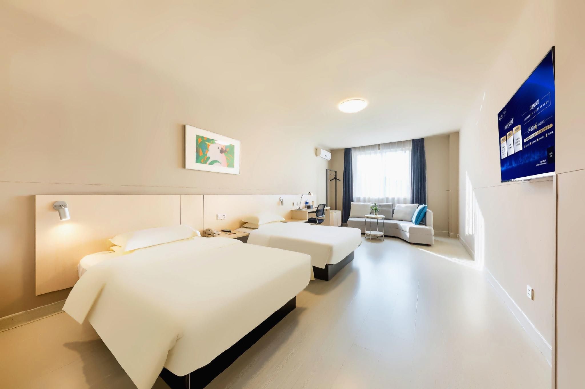 Habitación de hotel con dos camas, un escritorio, una silla, un sofá y un ventanal con cortinas.