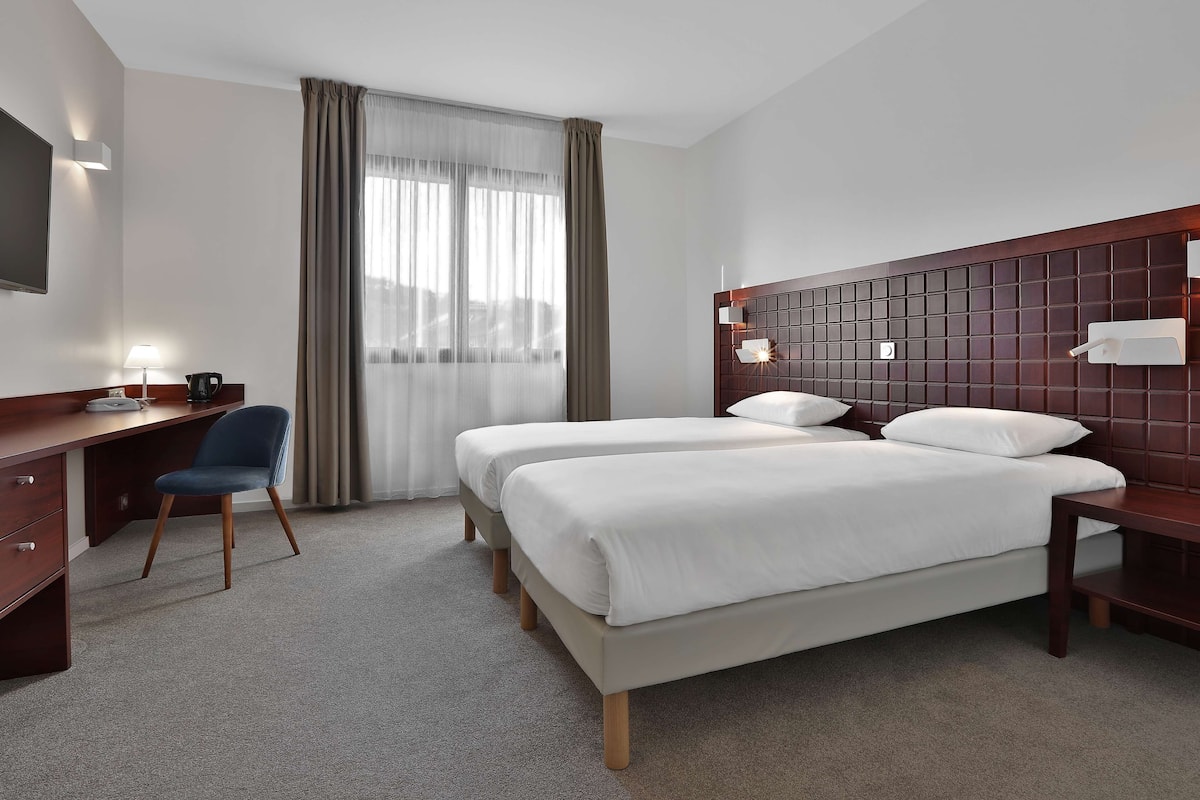 Ein Hotelzimmer mit Bett, Schreibtisch, Stuhl und einem großen Fenster mit Vorhängen.