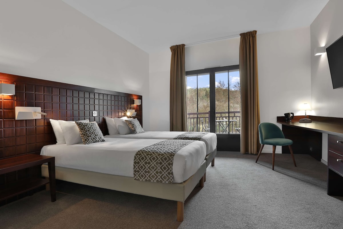 Ein Hotelzimmer mit einem großen Bett, einem Schreibtisch, einem Stuhl und einem an der Wand befestigten Fernseher.