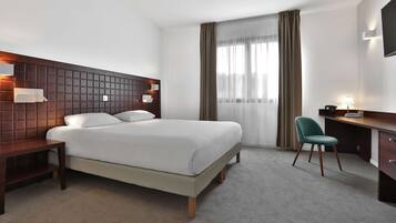 A modern hotel room with a large bed, a desk, a chair, and a TV mounted on the wall.