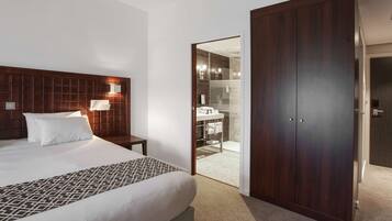 Une chambre d’hôtel avec un grand lit, une table de chevet, une armoire et une salle de bain visible à travers une porte ouverte.