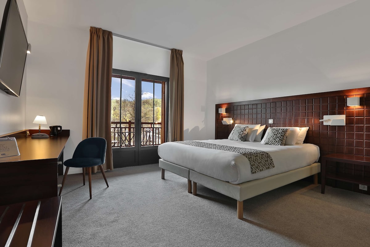 Ein Hotelzimmer mit einem Bett, einem Schreibtisch, einem Sessel, einem Fernseher und einem Fenster mit Vorhängen.