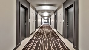 A long, narrow hotel corridor with doors on both sides, a patterned carpet, and recessed lighting on the ceiling.