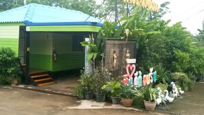 Un petit bâtiment vert, avec un toit bleu, une pancarte d’accueil et diverses plantes en pot.