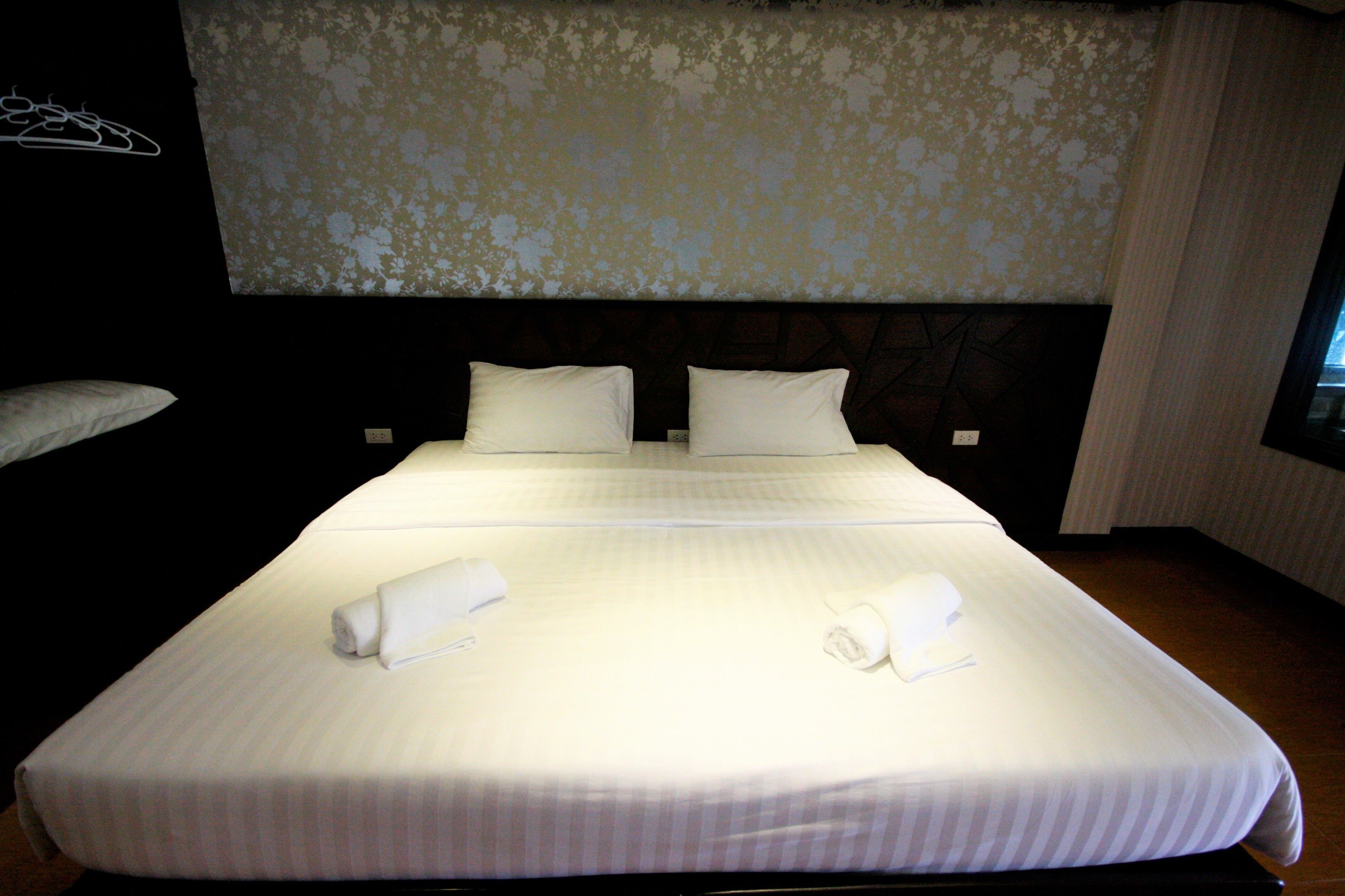 A neatly made bed with white linens and pillows, a headboard with a floral pattern, and a dark wooden headboard on the left.
