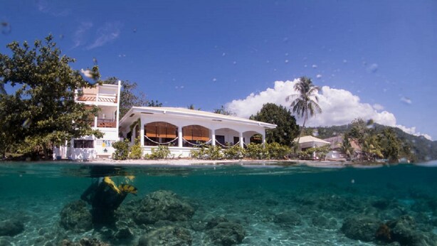 A beachfront property with a white building featuring a covered patio and a clear view of the ocean and rocky underwater terrain. - Sogod Bay Scuba Resort (Padre Burgos)