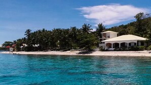 A beachfront property with a white building, a sandy beach, and palm trees. - Sogod Bay Scuba Resort (Padre Burgos)
