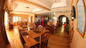A spacious dining area with wooden tables and chairs, a kitchen in the background, and a large map on the wall. - Sogod Bay Scuba Resort (Padre Burgos)