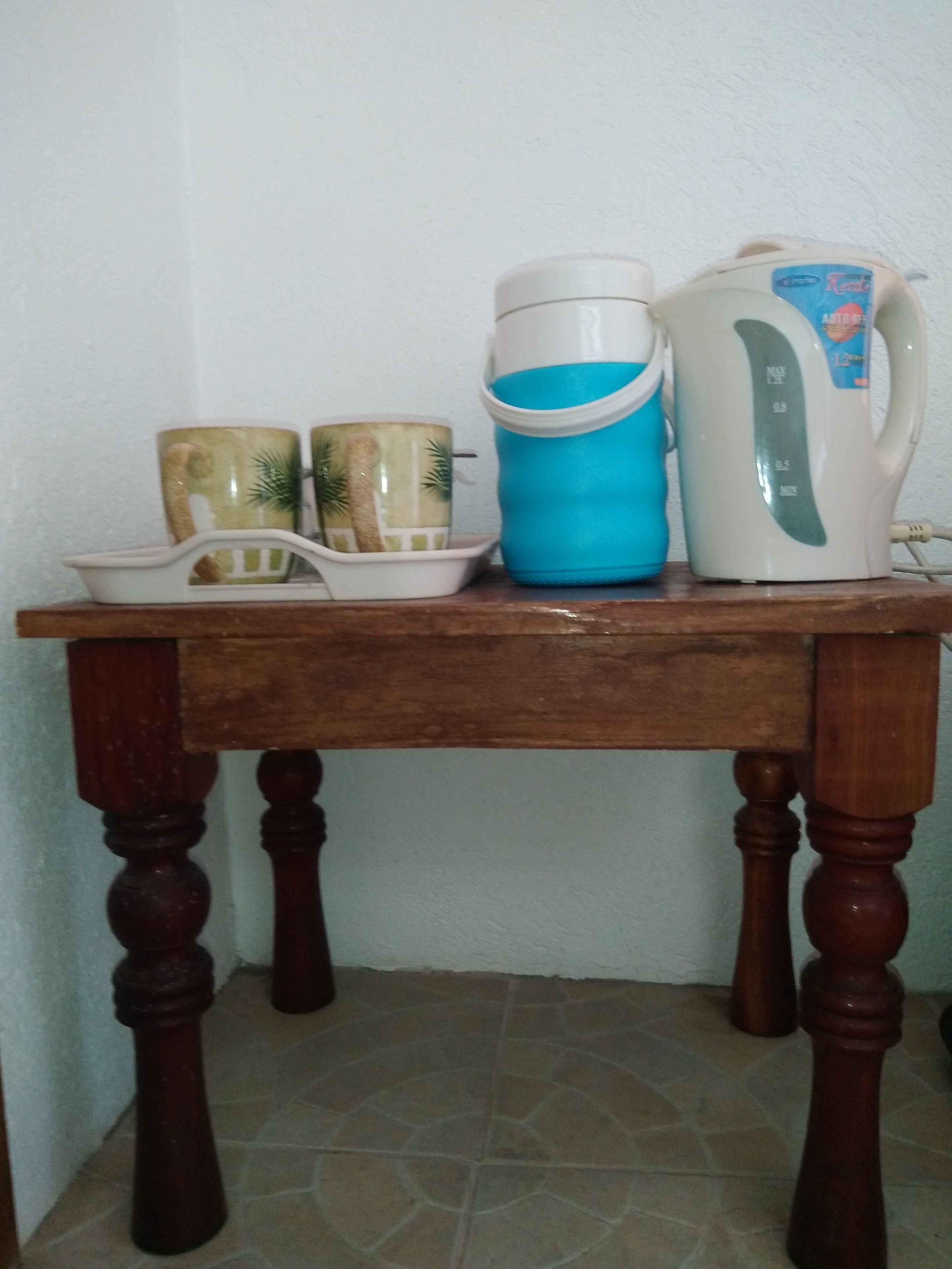 Ein Holztisch mit einer weißen Tasse, einer blauen Wasserflasche und einem weißen Wasserkocher.