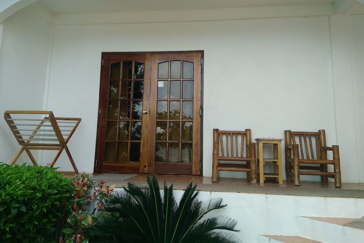 Un porche abrité avec une porte en bois, deux chaises en bois et une petite table.