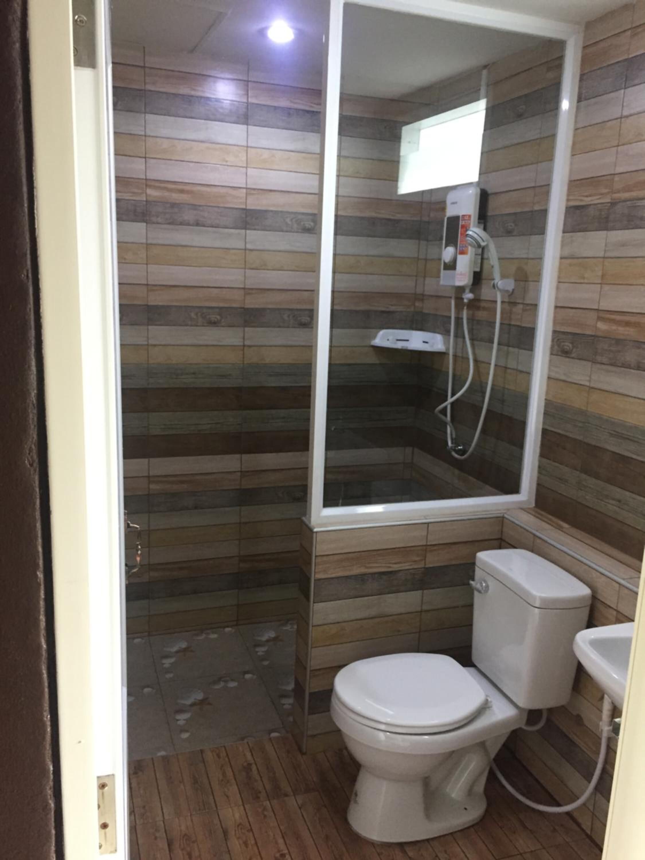 Un baño con piso de madera, inodoro, lavamanos y ducha con mampara de vidrio.