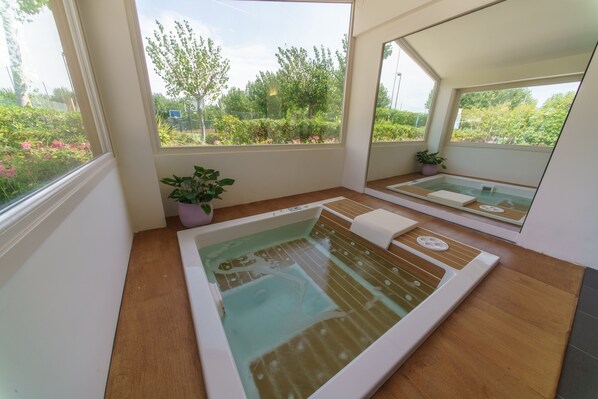 Ein Wellnessraum mit großem Fenster, Holzboden und einer kleinen Topfpflanze.