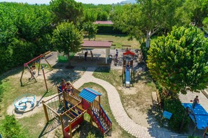 Ein Spielplatz mit verschiedenen Spielgeräten, einer überdachten Sitzgelegenheit und einem gepflasterten Weg.