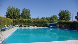 A swimming pool with clear blue water, surrounded by white lounge chairs and a tiled deck. - Centro Vacanze Camping Spinnaker (Fermo)