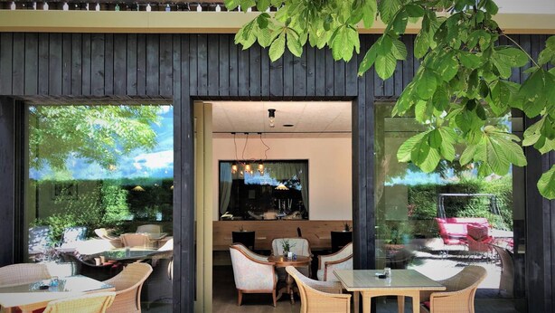 An outdoor seating area with wicker furniture and glass tables, overlooking a garden and a pool.