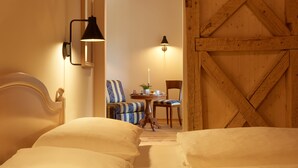 A hotel room with two beds, a wooden wall, a dining table with chairs, and two wall-mounted lamps.