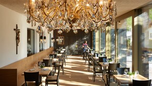 A restaurant interior with a large chandelier, wooden tables, and chairs.