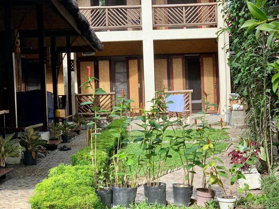 A two-story building with a covered patio area, potted plants, and a stone pathway.