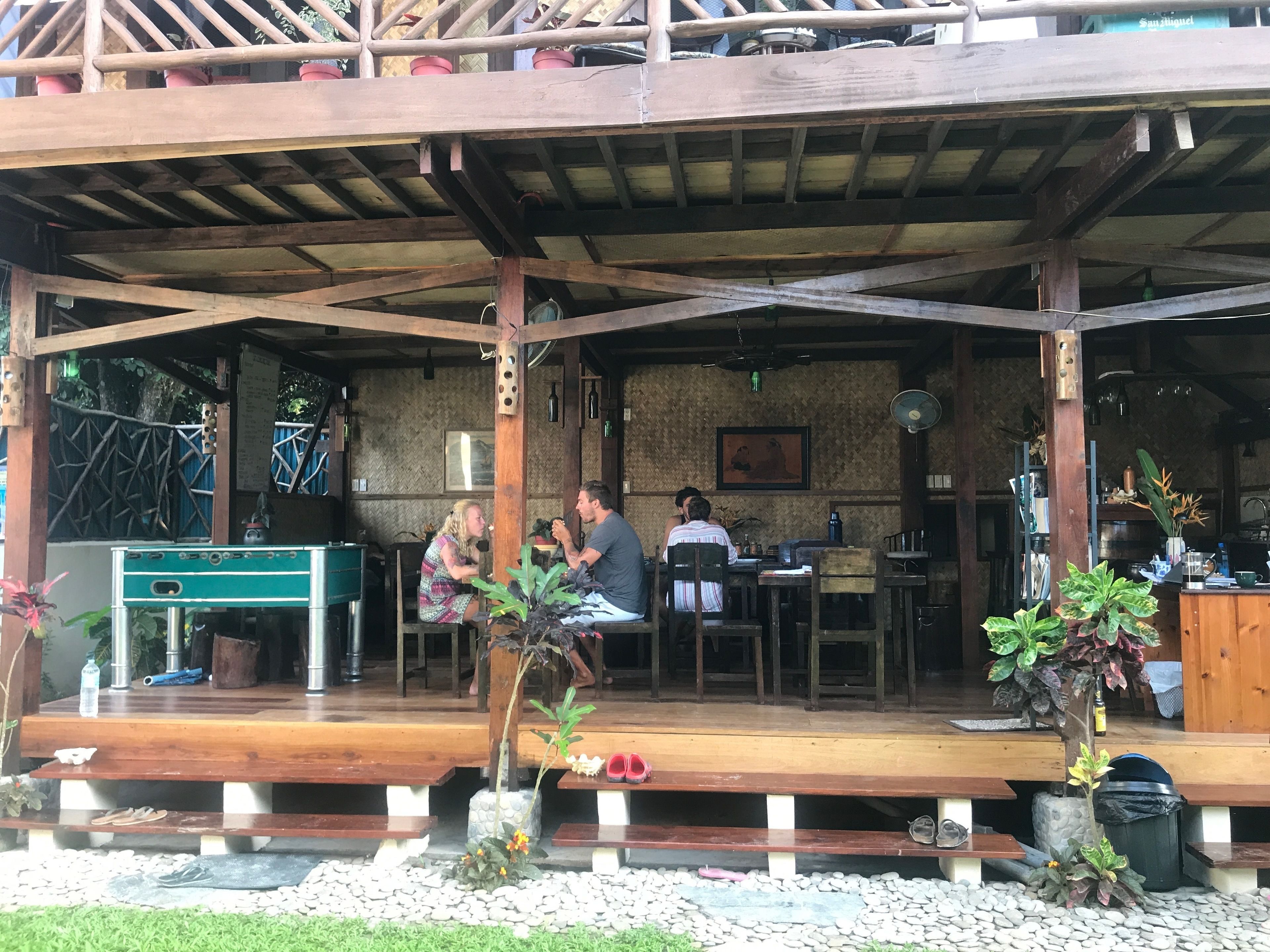 A wooden outdoor seating area with tables and chairs, a small stage, and a few potted plants.