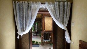 Ein Hotelzimmer mit Bett, weißen Vorhängen und Blick auf einen Außenbereich mit Sitzgelegenheiten.