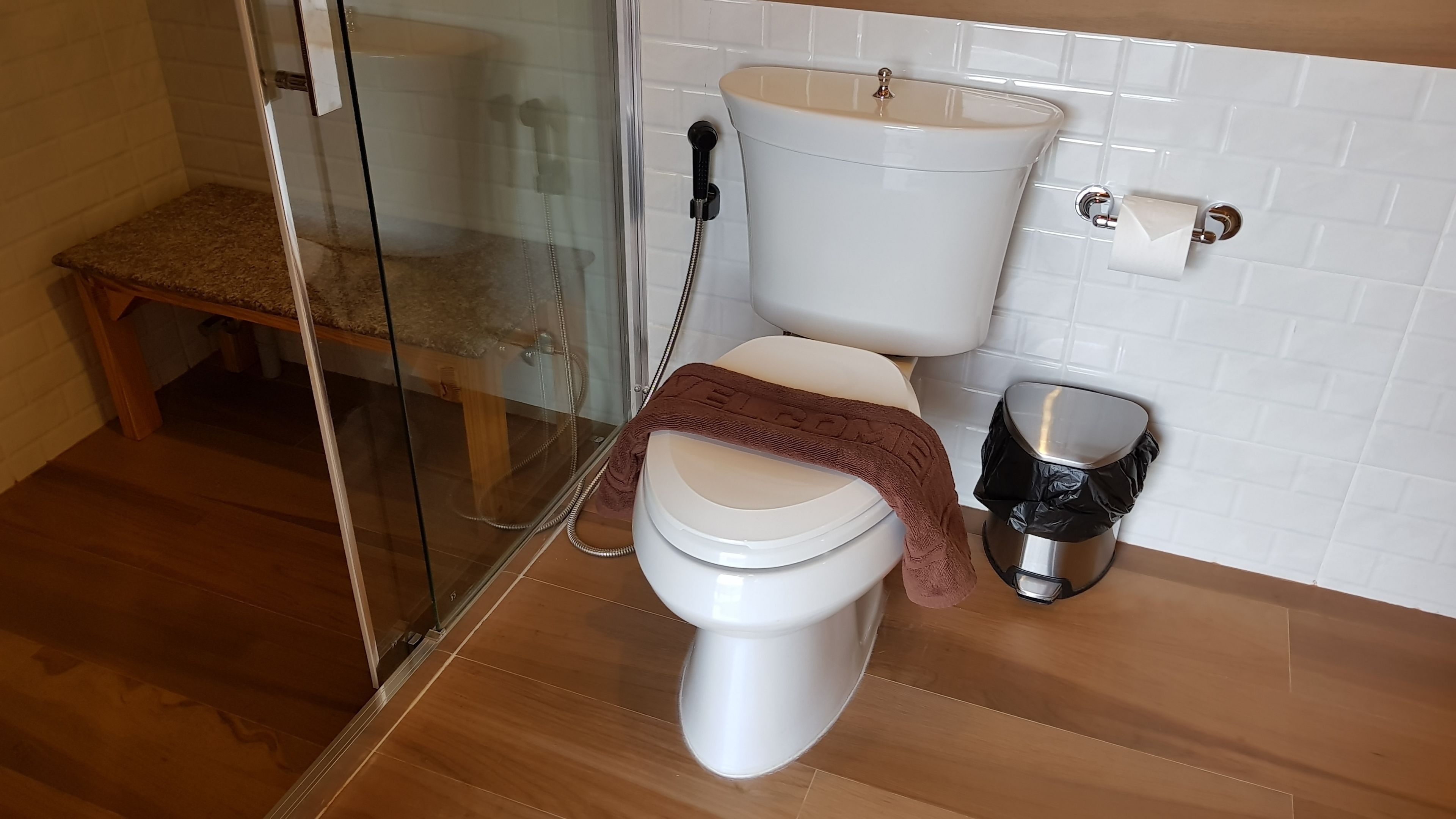 Un baño con inodoro, cabina de ducha de vidrio y banco de madera.