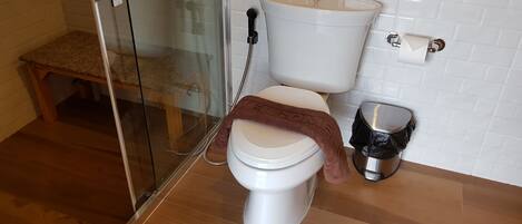 A bathroom with a toilet, a glass shower enclosure, and a wooden bench.