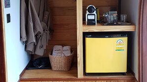 A compact room with a wooden floor, a yellow refrigerator, a fan, a basket, and slippers. - Kiripura Resort (Khao Kho)