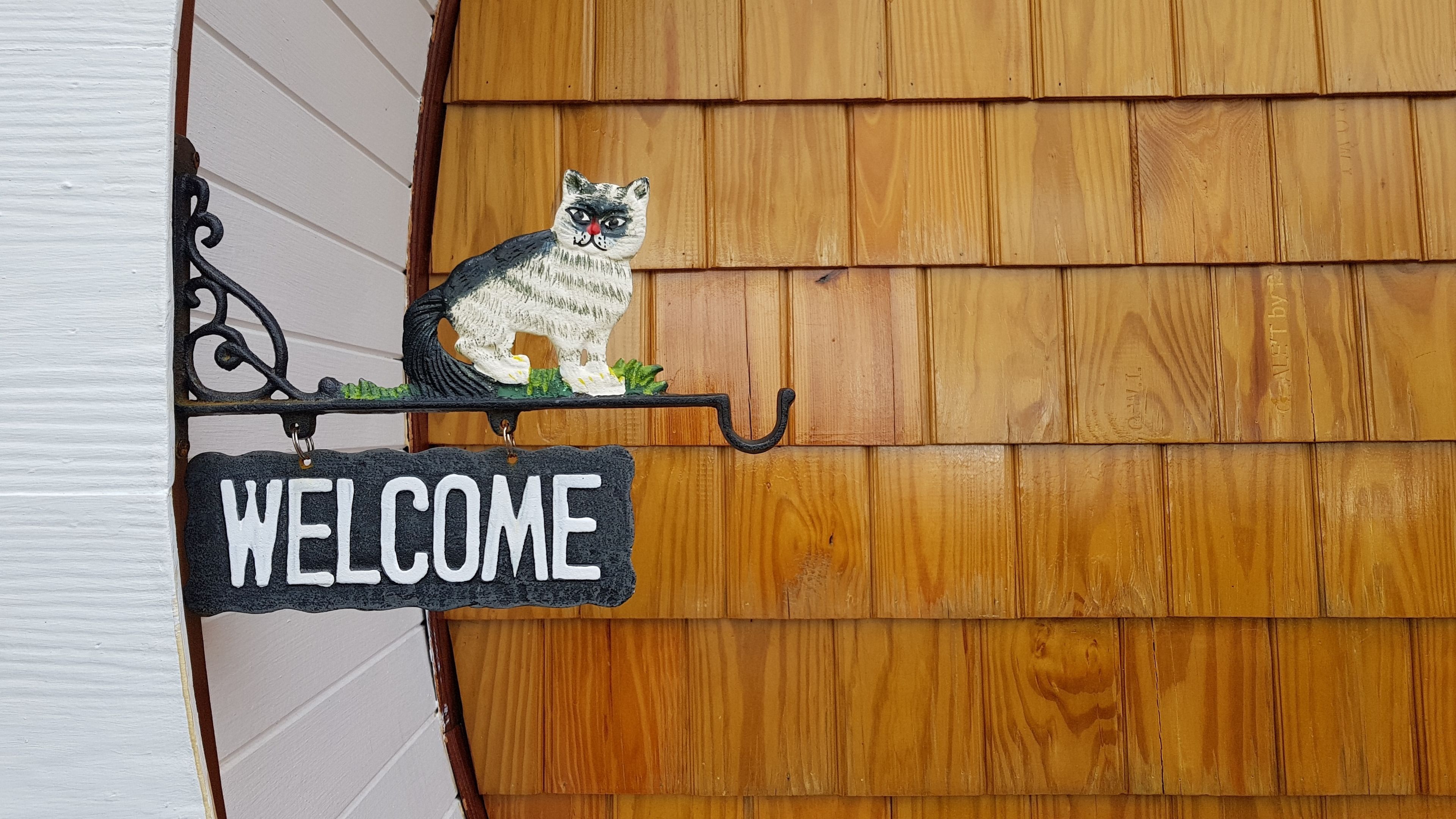 A welcome sign with a raccoon illustration mounted on a metal bracket against a wooden wall.