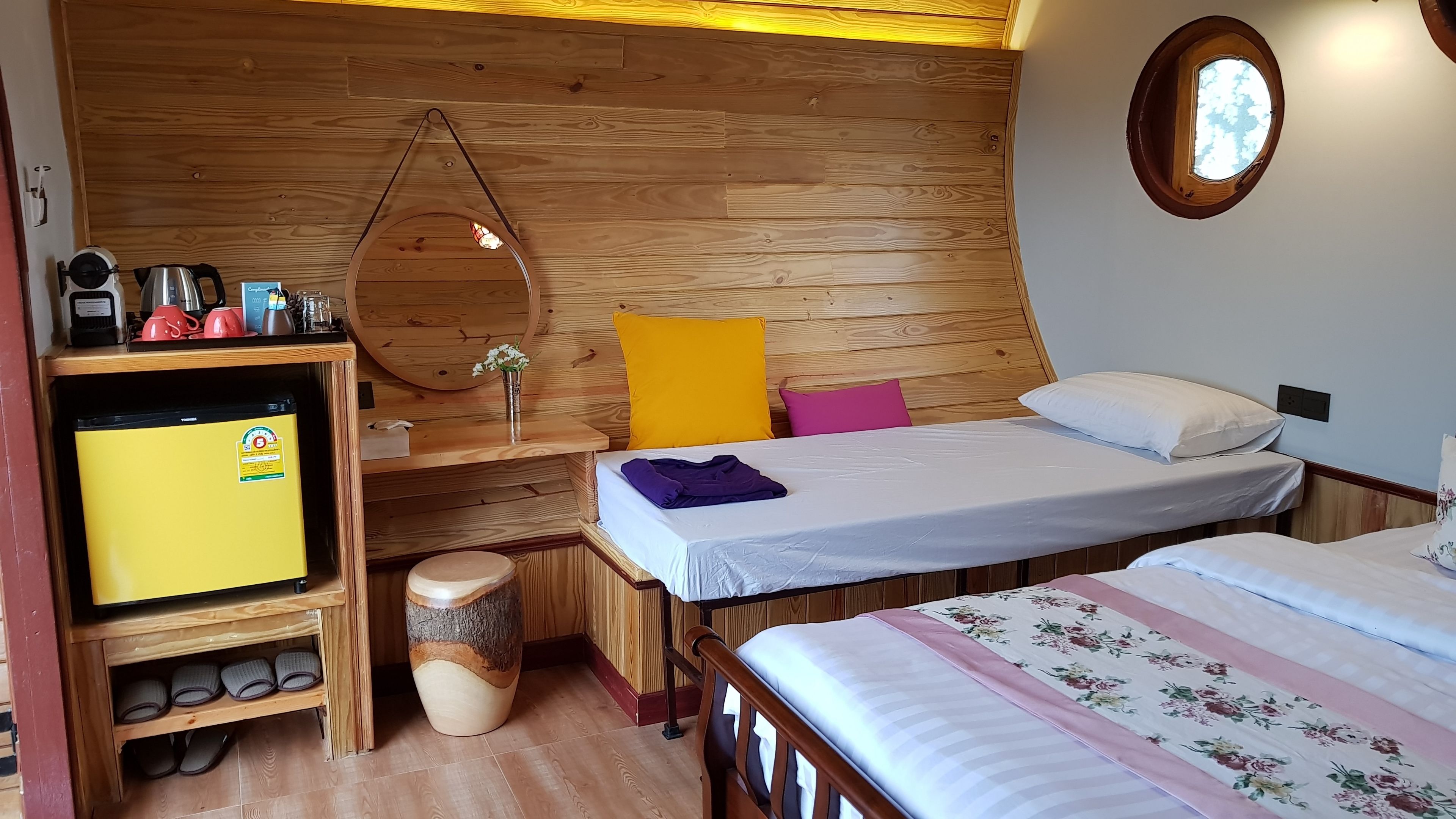 Una habitación acogedora con techo de madera, una cama con colcha estampada, una mesita con una tetera y un armario de madera con zapatos.