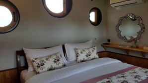 A neatly made bed with floral pillows, a wooden headboard, and a bedside table with a vase of flowers. - Kiripura Resort (Khao Kho)