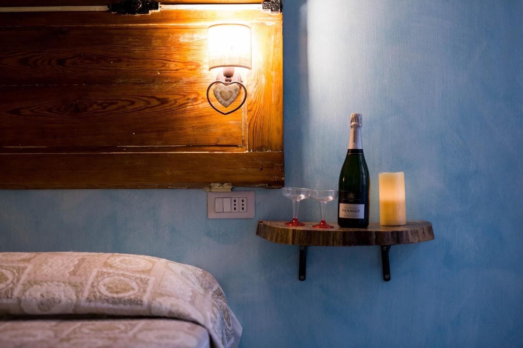 Une chambre à coucher avec une tête de lit en bois, une table de chevet sur laquelle se trouvent une bouteille de vin, deux verres et une bougie.