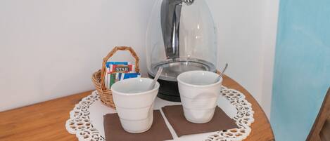 Una cafetera, dos tazas blancas, una cesta con un producto de Star y un mantel individual sobre una mesa de madera.